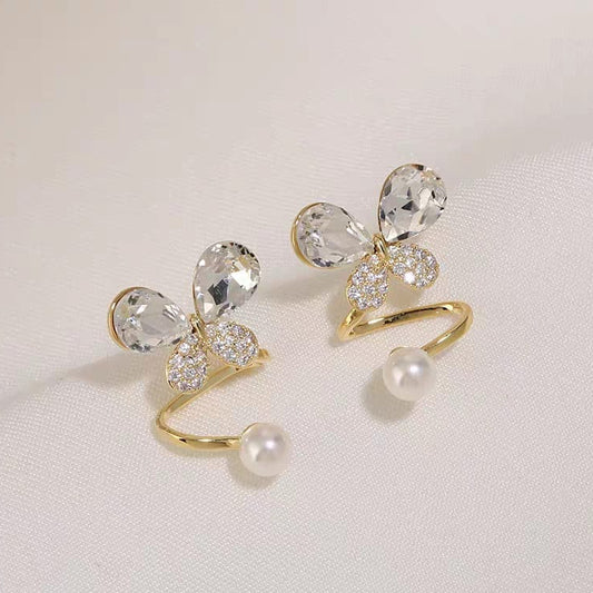 Gold bow-shaped earrings with clear crystals and a pearl on a light background