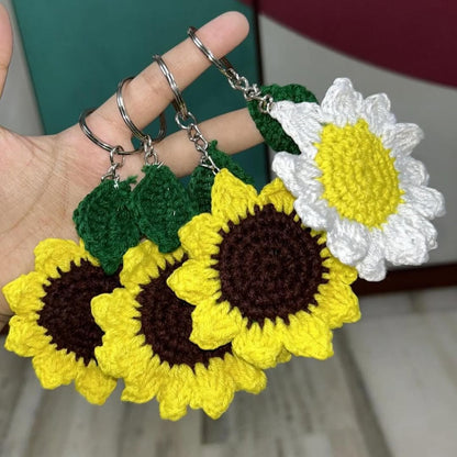 Hand holding three crocheted flower keychains in yellow, brown, green, and white.