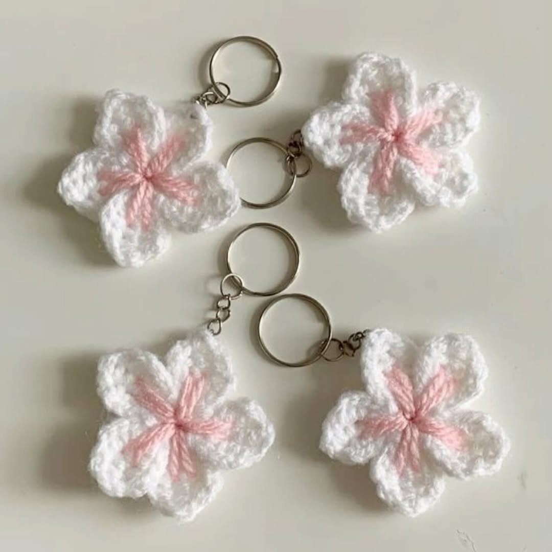 Four white and pink crocheted flower keychains on a light background