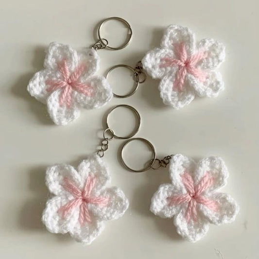 Four white and pink crocheted flower keychains on a light background