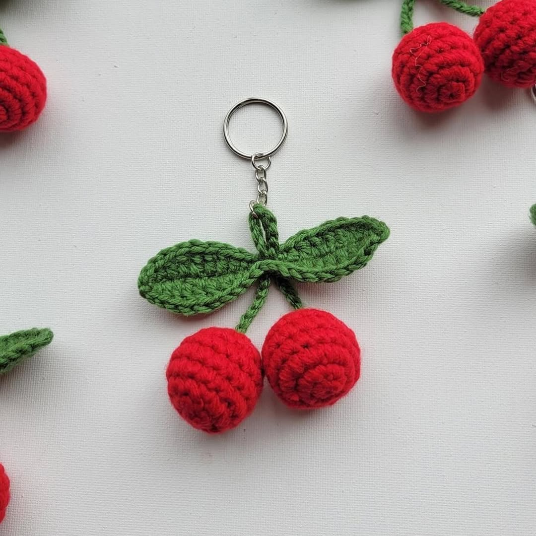 Crocheted red berry keychain with green leaves on a white background