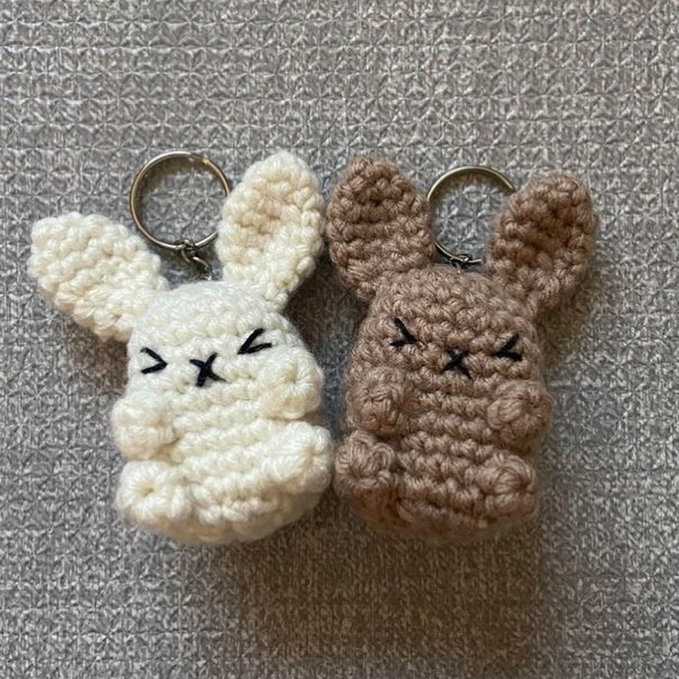 Two crocheted bunny keychains, one white and one brown, on a textured gray background.
