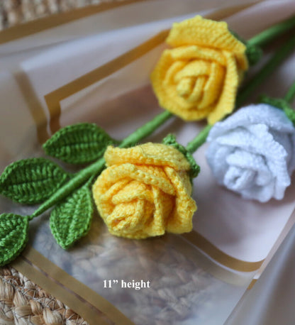 Three crocheted roses in yellow, white, and green on a textured surface.