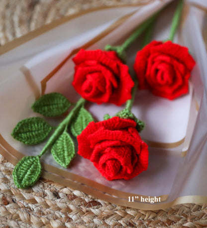 Three red crocheted roses with green leaves on a textured surface.